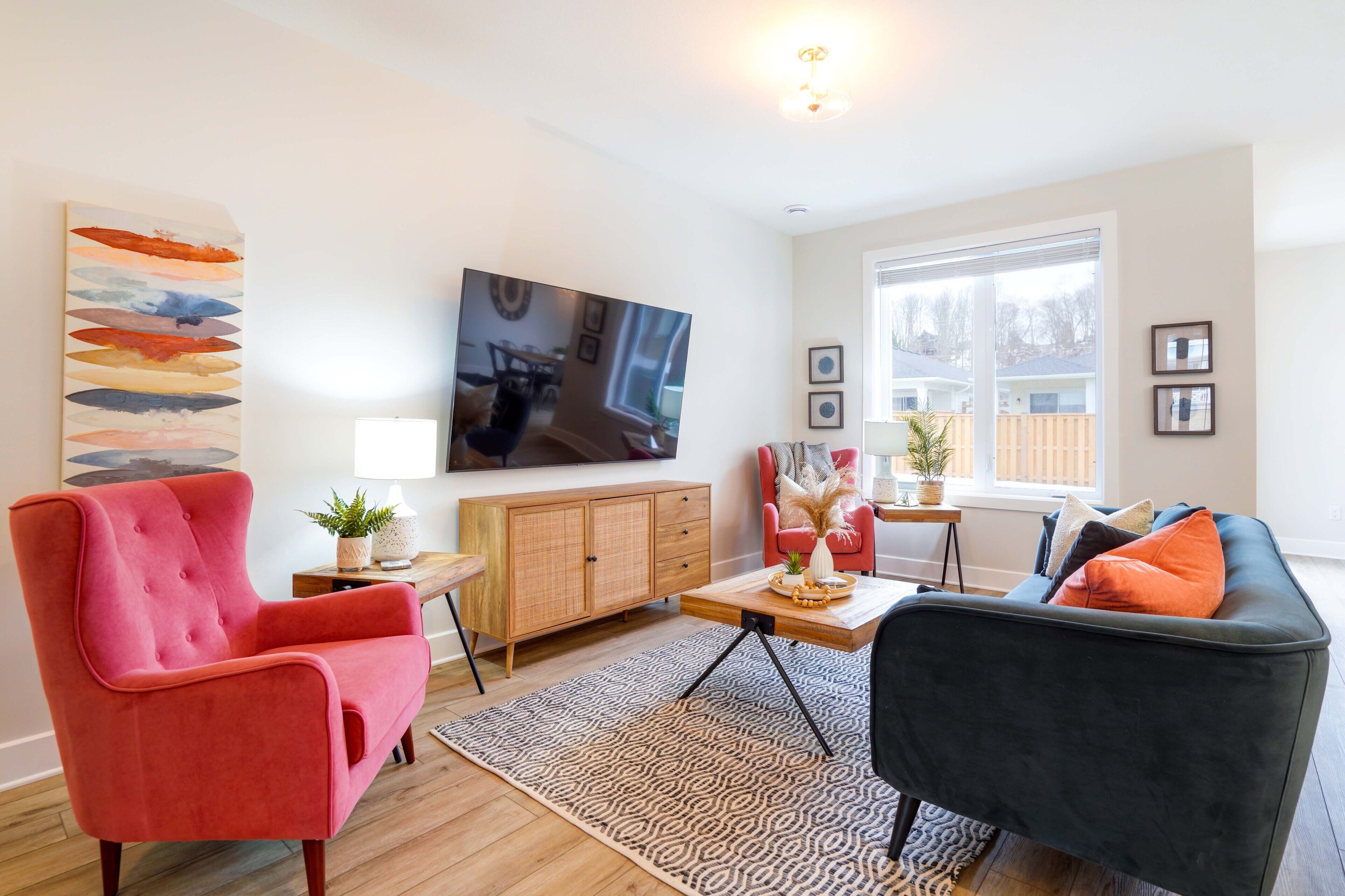 A living room with a red armchair, a black sofa, a wooden cabinet, a TV on the wall, and a large window.