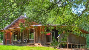 A rustic wooden cabin with a porch, a covered deck, and a small outdoor seating area.
