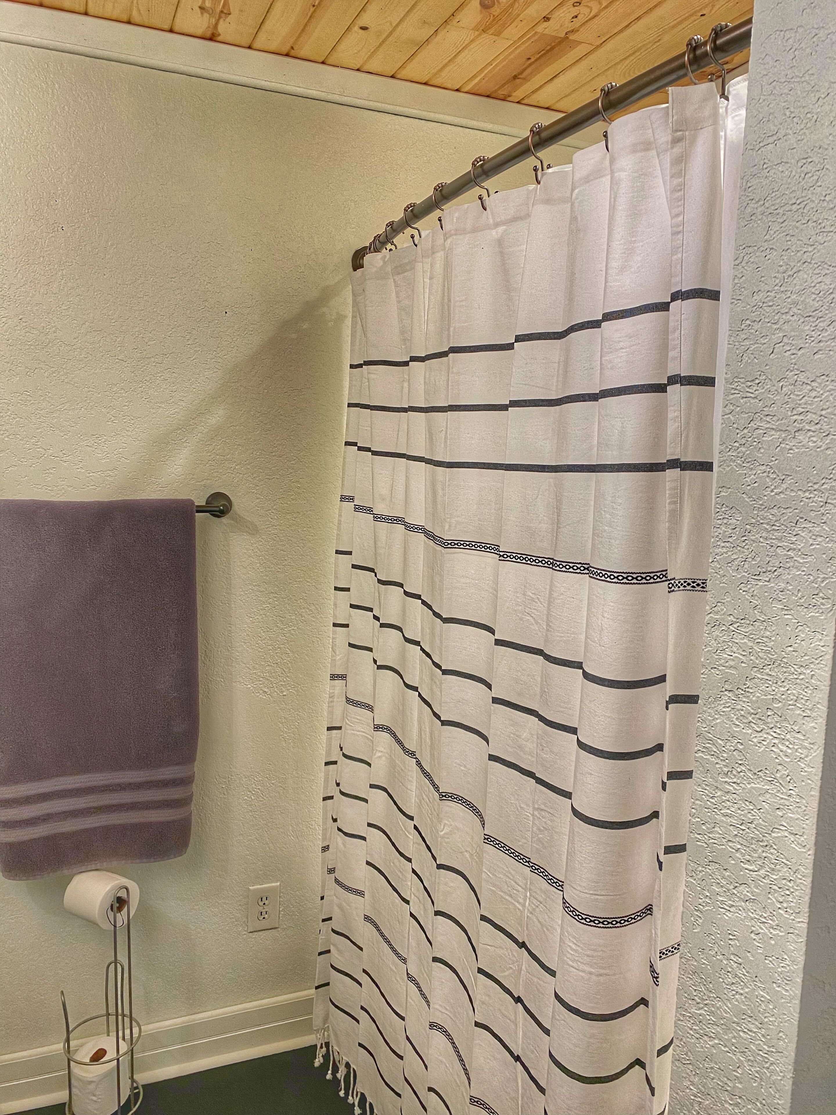 A bathroom with a striped shower curtain, a purple towel, and a paper towel holder.