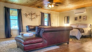 A spacious living room with a leather sofa, a wooden ceiling, and a bed in the background.