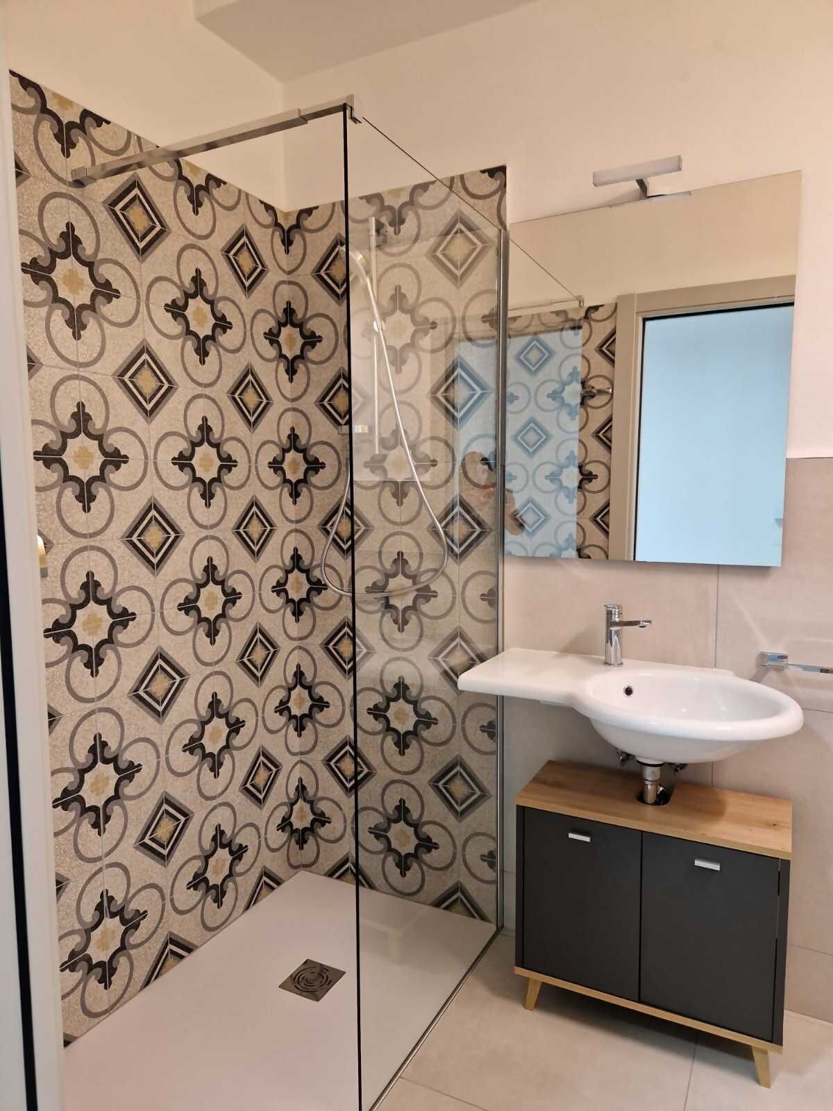 A modern bathroom with a glass shower enclosure, a white sink, and a dark cabinet.