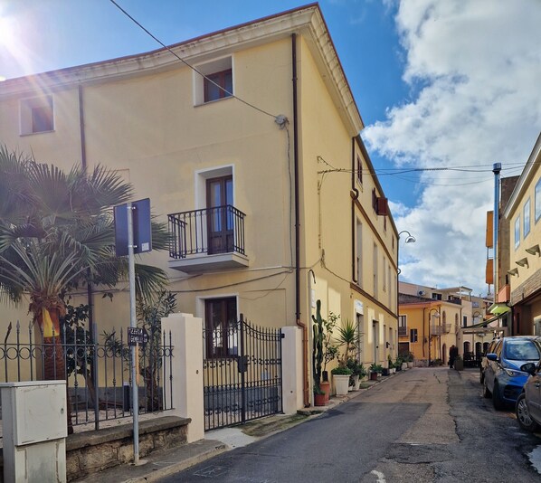 A narrow street with yellow buildings, a metal gate, and a parked car.