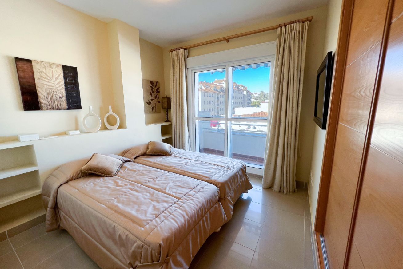 Habitació d'hotel amb dos llits, una finestra gran amb cortines, un balcó i vista a edificis.