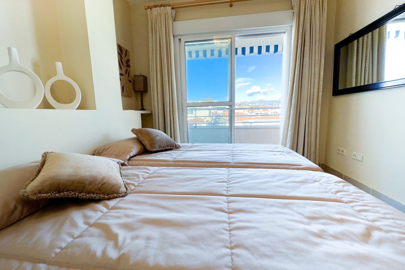 Ein Hotelzimmer mit einem großen Bett, zwei Kissen, einem Fenster mit Vorhängen und Blick auf die Stadt.