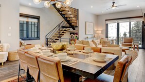 Un espace de repas moderne avec une table centrale dressée pour un repas, entourée de sièges confortables. Un escalier avec une rampe noire mène à un niveau supérieur.