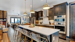Une cuisine moderne dotée d’appareils électroménagers en acier inoxydable, d’un grand îlot central avec des tabourets, et de meubles de rangement en bois foncé.