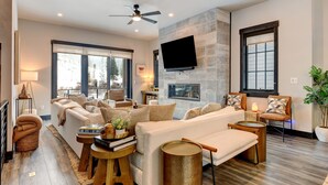 Un salon moderne avec un ensemble de canapés, un téléviseur à écran plat fixé au mur et un ventilateur de plafond.