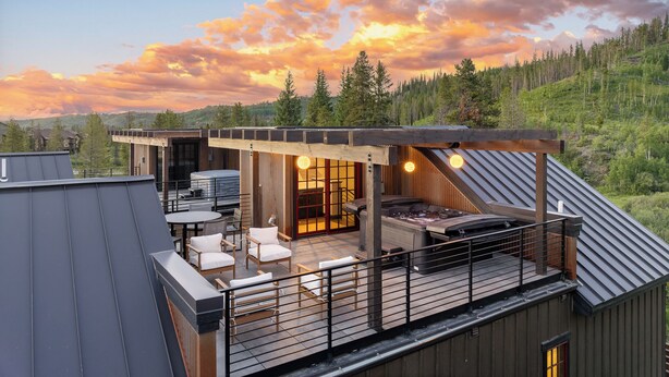 Une terrasse extérieure moderne, dotée d’un espace salon et d’un jacuzzi, offrant une vue sur une colline boisée.