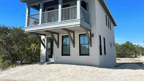 A two-story house with a balcony, large windows, and a gravel driveway.