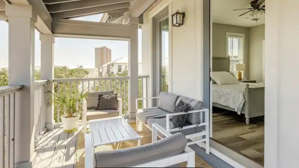 A balcony with a white railing, a sofa, a chair, and a potted plant.