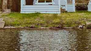 Une maison avec un porche, un banc et un petit quai qui s’avance sur une étendue d’eau.
