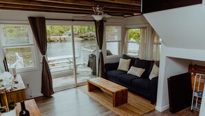 Un salon moderne avec un canapé foncé, une table basse en bois et une vue sur un plan d’eau grâce à de grandes portes-fenêtres coulissantes.