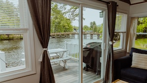 Une pièce dotée d’une porte-fenêtre coulissante donnant sur une terrasse avec un barbecue, une table blanche et un canapé noir agrémenté d’un coussin.