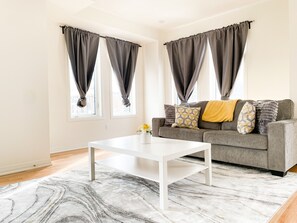 Uma sala de estar com um sofá cinzento, uma mesa de centro branca e um tapete estampado.