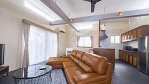 A modern living room with a sectional sofa, a glass coffee table, and a dining area with a kitchen in the background.