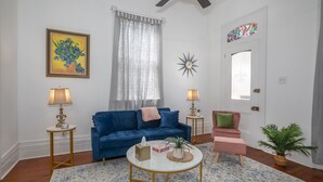 Un salón con sofá azul, una mesa redonda de centro, dos lámparas, una planta en maceta y una puerta con un vitral.
