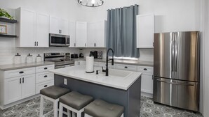 Una cocina moderna con armarios blancos, un refrigerador de acero inoxidable, una isla central con taburetes y un piso estampado.