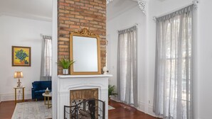 Una sala de estar con chimenea, un sofá azul, una mesita con una lámpara y un espejo grande sobre la chimenea.