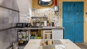 A compact kitchen with a microwave, toaster, and sink. There's a small refrigerator and a blue door in the background. - Casetta PesceBlu, a stay with a unique style (Trieste)