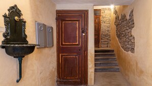 A hallway with a wooden door, a stone wall, and a metal wall-mounted fixture. - Casetta PesceBlu, a stay with a unique style (Trieste)