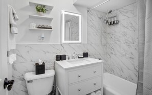 A modern bathroom with a white sink, toilet, and bathtub. There are shelves with toiletries and a mirror above the sink. - Chicago charm! Quiet and inviting ! (Chicago)