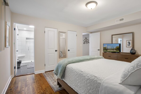 A bedroom with a large bed, a television, and a bathroom visible through an open door. - Chicago charm! Quiet and inviting ! (Chicago)
