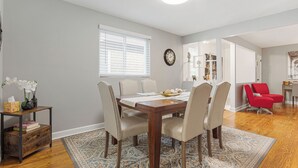 Un coin repas avec une table en bois, des chaises beiges, un tapis à motifs et une fenêtre avec des stores.