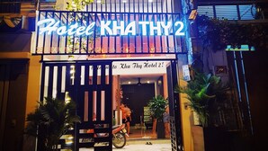 La entrada del Hotel Kha Thuy 2, con un letrero de neón, una motocicleta estacionada y plantas en macetas.