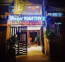 La entrada del Hotel Kha Thuy 2, con un letrero de neón, una motocicleta estacionada y plantas en macetas.