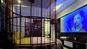 Una habitación moderna con una zona de estar curva y cerrada, una pantalla de televisión y un baño a la vista al fondo.