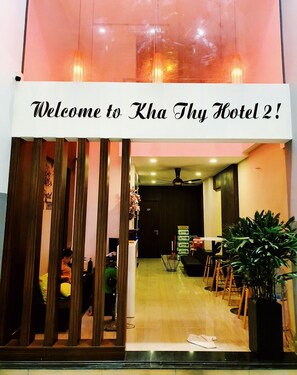 La entrada del hotel Kha Thy 2, con un mostrador de recepción, zona de estar y una planta grande en maceta.