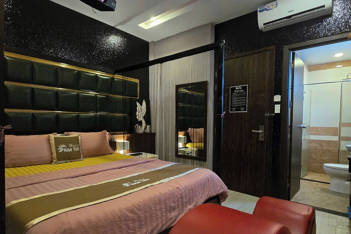 Una habitación de hotel con una cama grande, un sillón de cuero rojo, una mesita de noche y un armario.