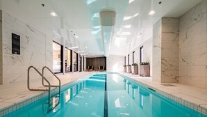 Una piscina interna con acqua cristallina, circondata da pareti con motivi in marmo e dotata di corrimano in metallo.