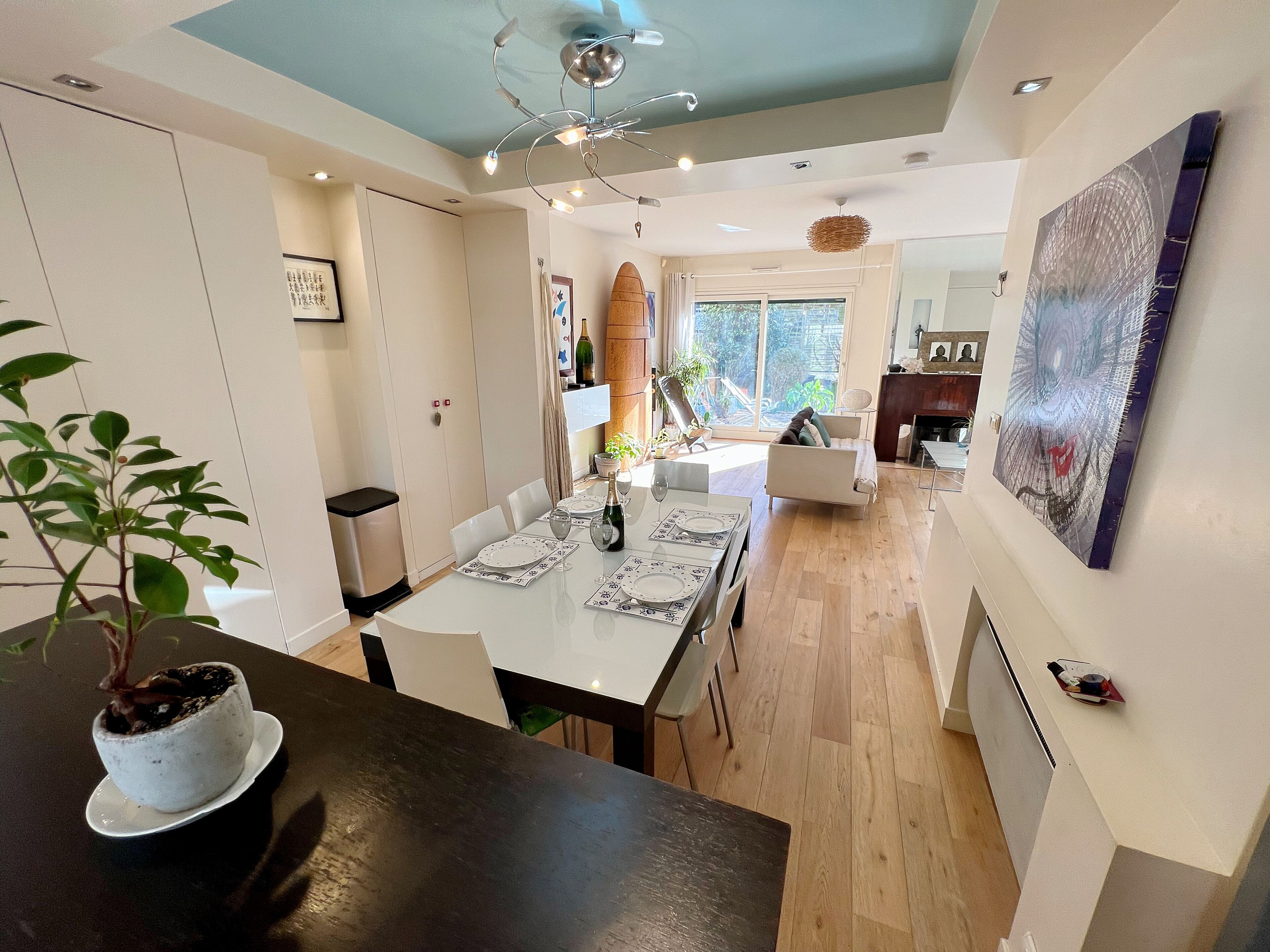 Een moderne eethoek met een witte tafel gedekt voor vier personen, een kroonluchter en uitzicht op het omliggende landschap door een groot raam.