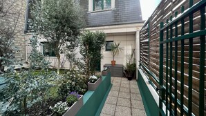 A narrow courtyard with a tiled floor, surrounded by buildings with a mix of stone and brick facades. There are several potted plants and a small tree in the center. - Splendid House, Jacuzzi and Private Gardens Paris (Boulogne-Billancourt)