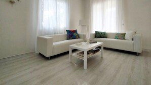 A modern living room with two white sofas, a white coffee table, and sheer white curtains.