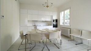 A modern kitchen with white cabinets, a built-in oven, and a dining area with a round table and chairs.