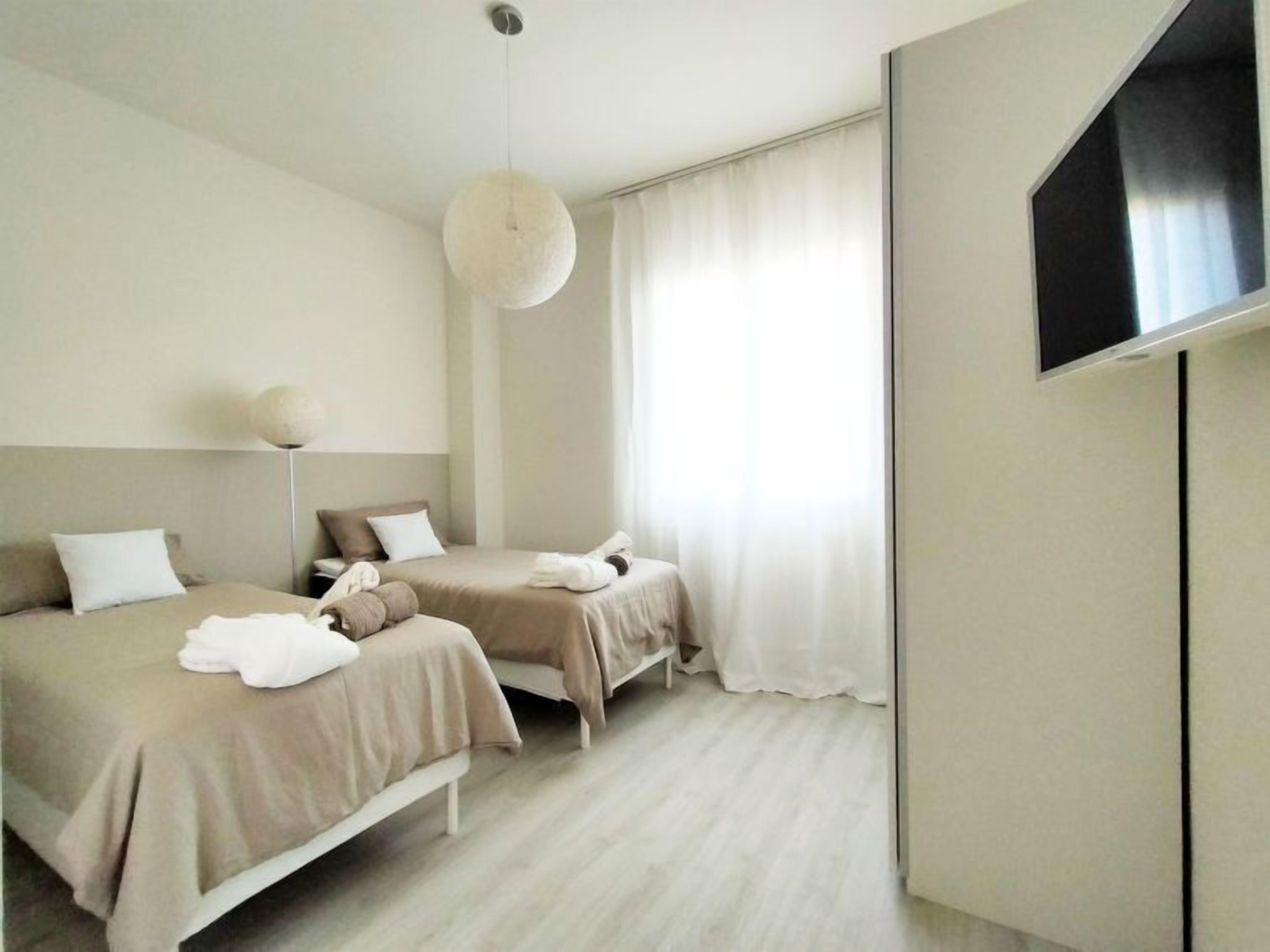 Ein Hotelzimmer mit zwei Betten, einem großen Spiegel, einem Flachbildfernseher und einem großen Fenster mit leicht transparenten Vorhängen.