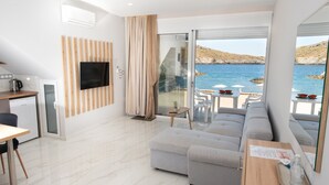 A modern living room with a sofa, a TV, a dining area, and a view of the sea. - Beachfront Studio Kyma East (Faistos)