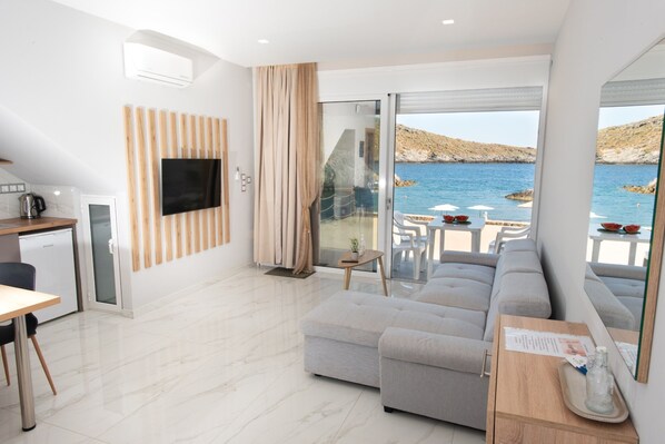 Una sala moderna con sofá, televisor, comedor y vista al mar.