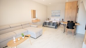 A modern hotel room with a sofa, a bed, a desk, and a dining area. - Beachfront Studio Kyma East (Faistos)