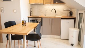 A compact kitchen with a wooden countertop, a sink, a stove, and a dishwasher. There is a dining table with chairs and a trash bin. - Beachfront Studio Kyma East (Faistos)