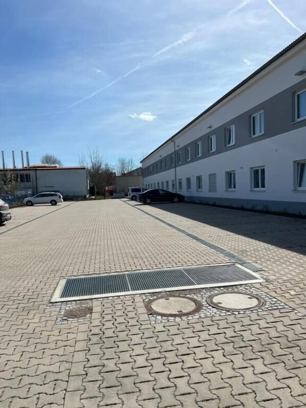 A paved walkway leading to a building with multiple windows and a ventilation grate. - Bordinghaus MDS (Aschheim)