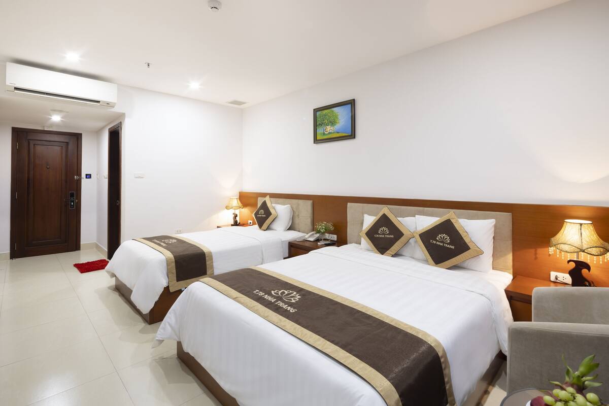 A hotel room with two beds, a wooden door, a small table with fruit, and a painting on the wall.