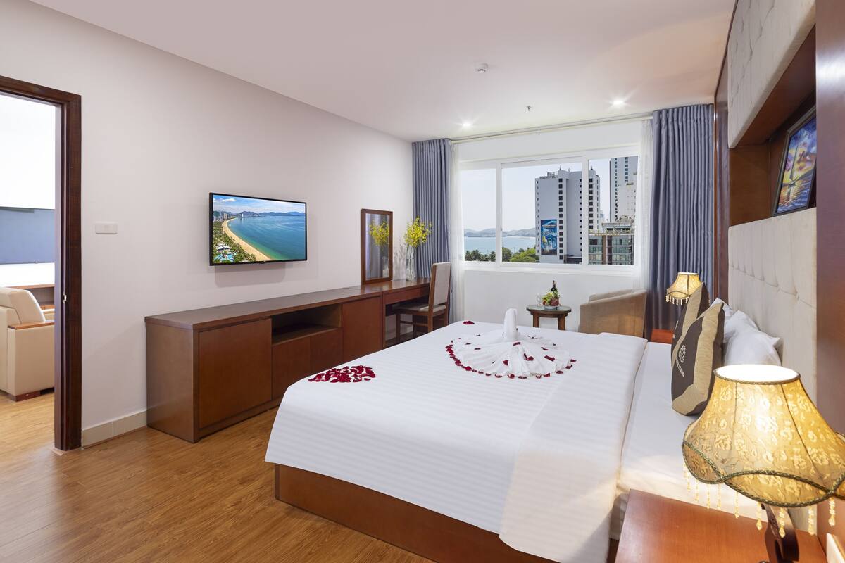 A hotel room with a large bed, a desk, a television, and a view of the cityscape.