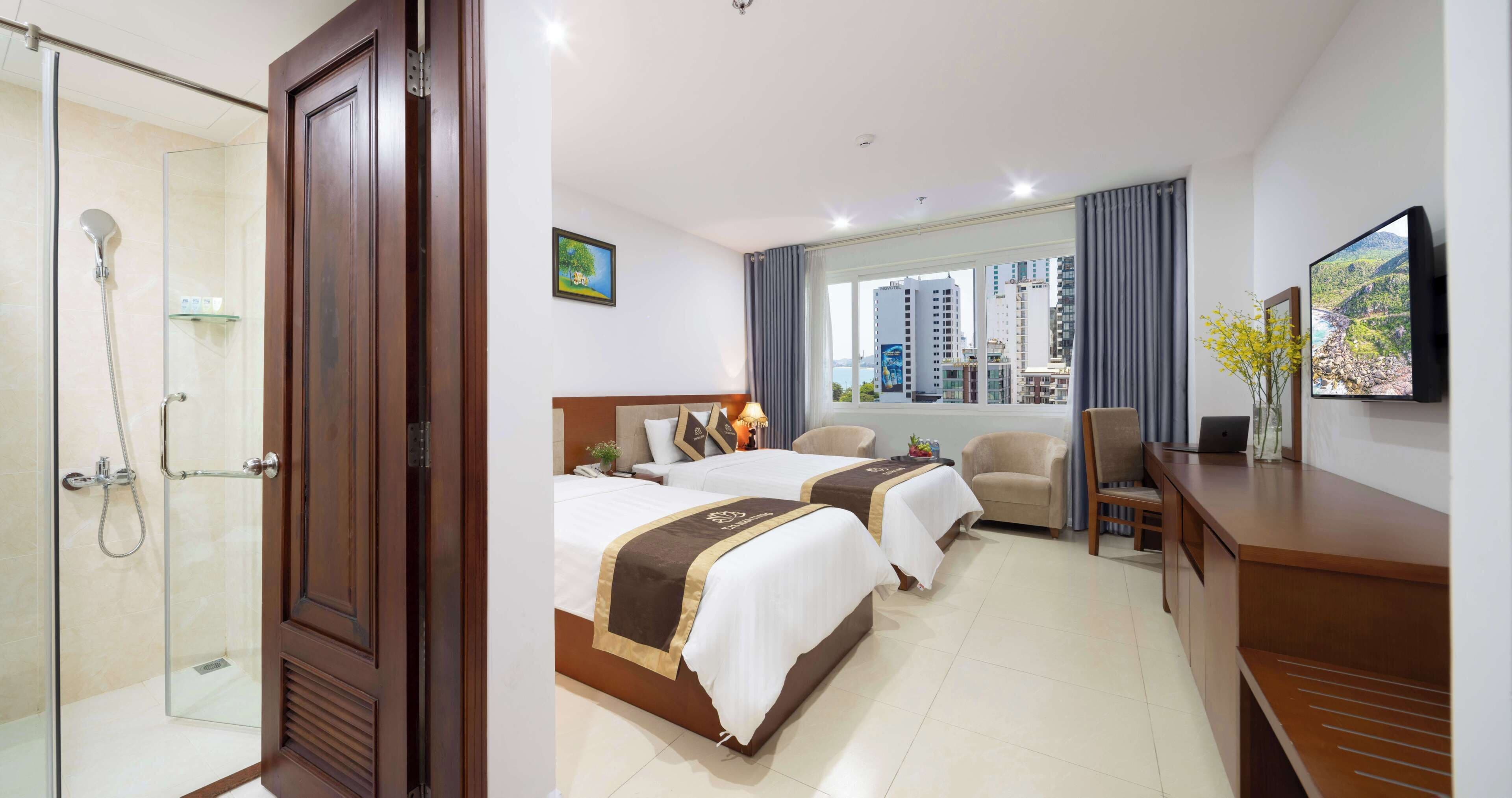 Habitación de hotel con ducha, dos camas, escritorio, silla y televisión.