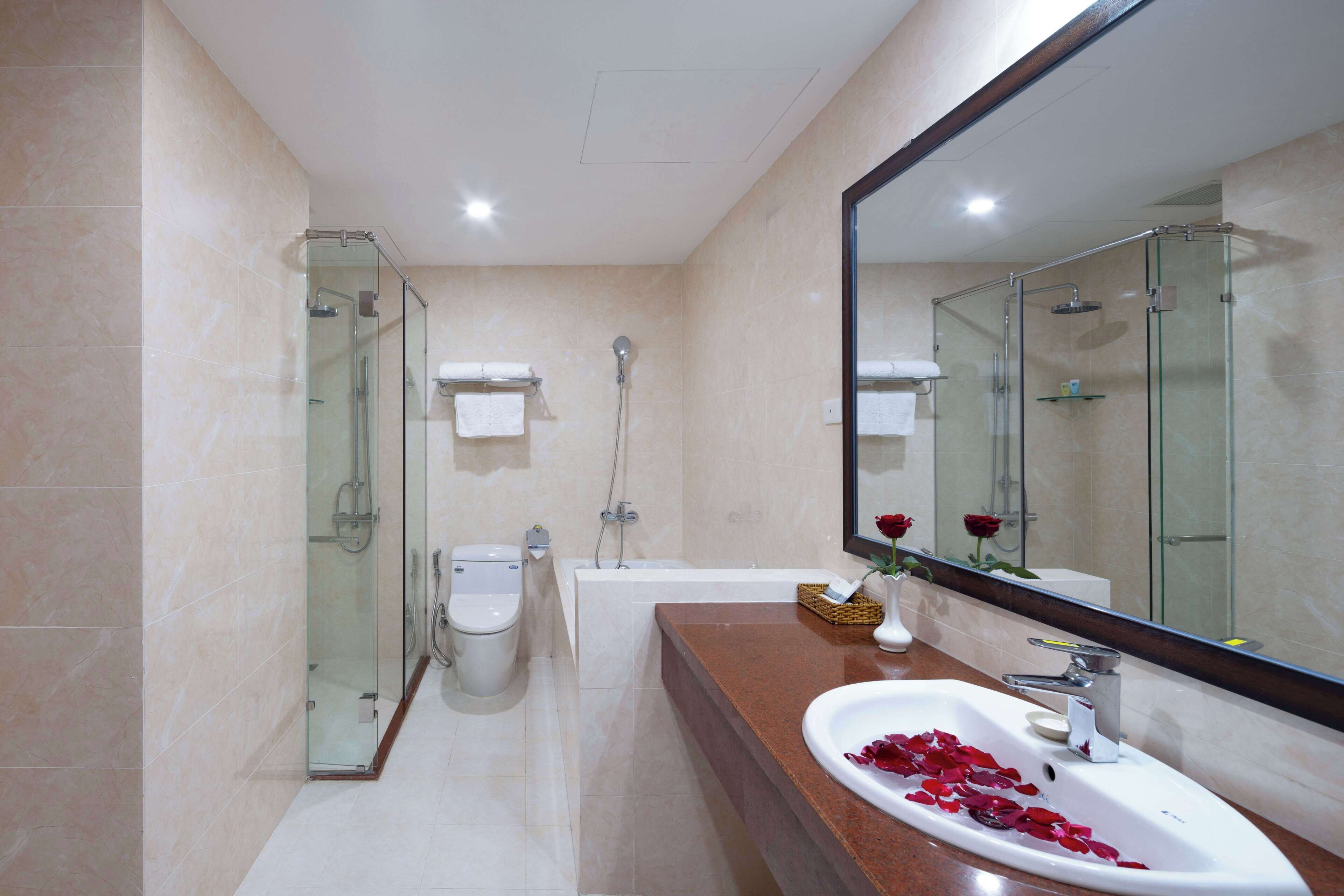 A modern bathroom with a glass-enclosed shower, a bathtub, a toilet, and a sink with rose petals.