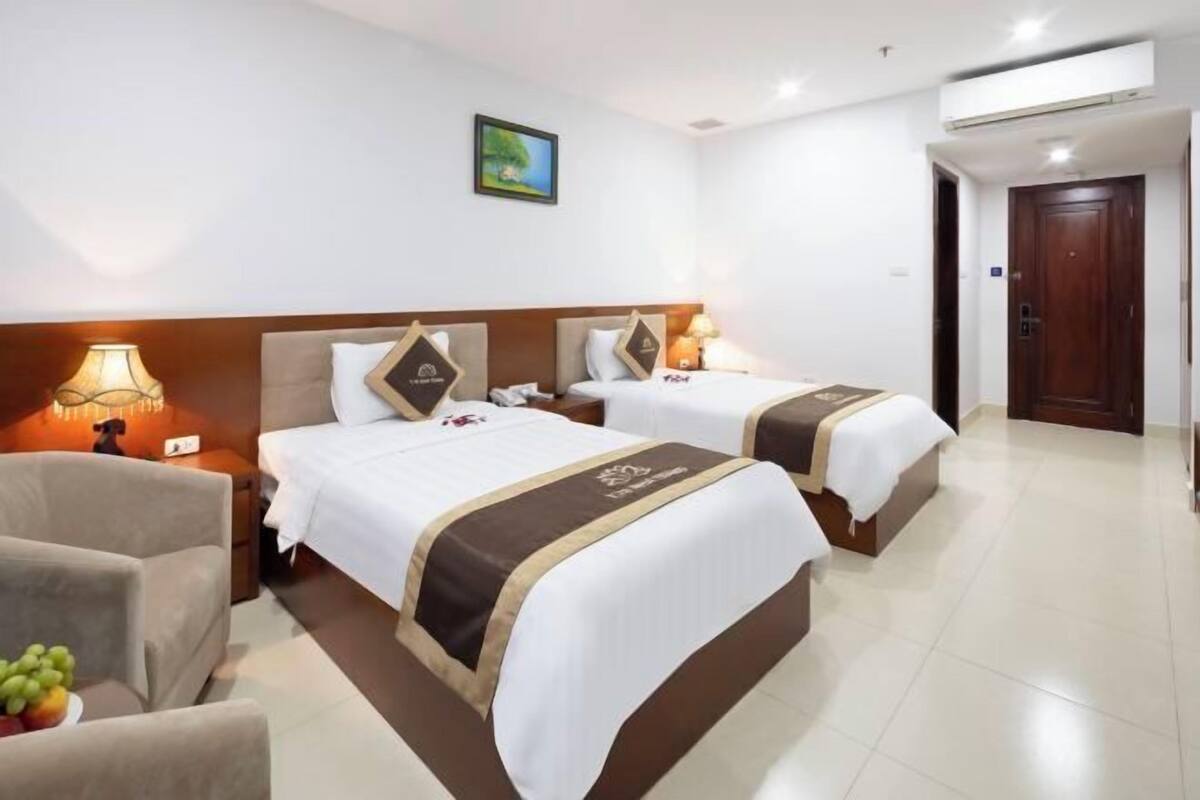A hotel room with two beds, a sofa, a lamp, and a fruit bowl.