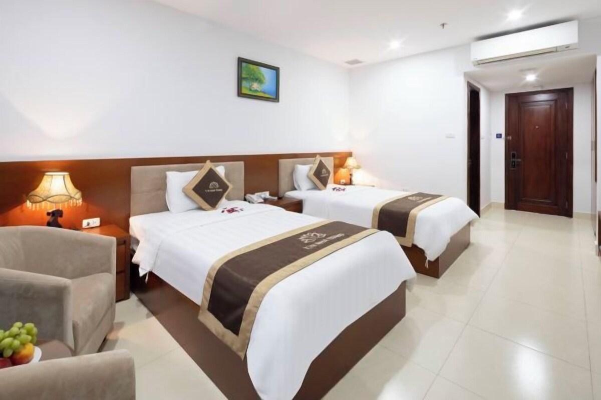 Une chambre d’hôtel avec deux lits, un canapé, une lampe et un panier de fruits.
