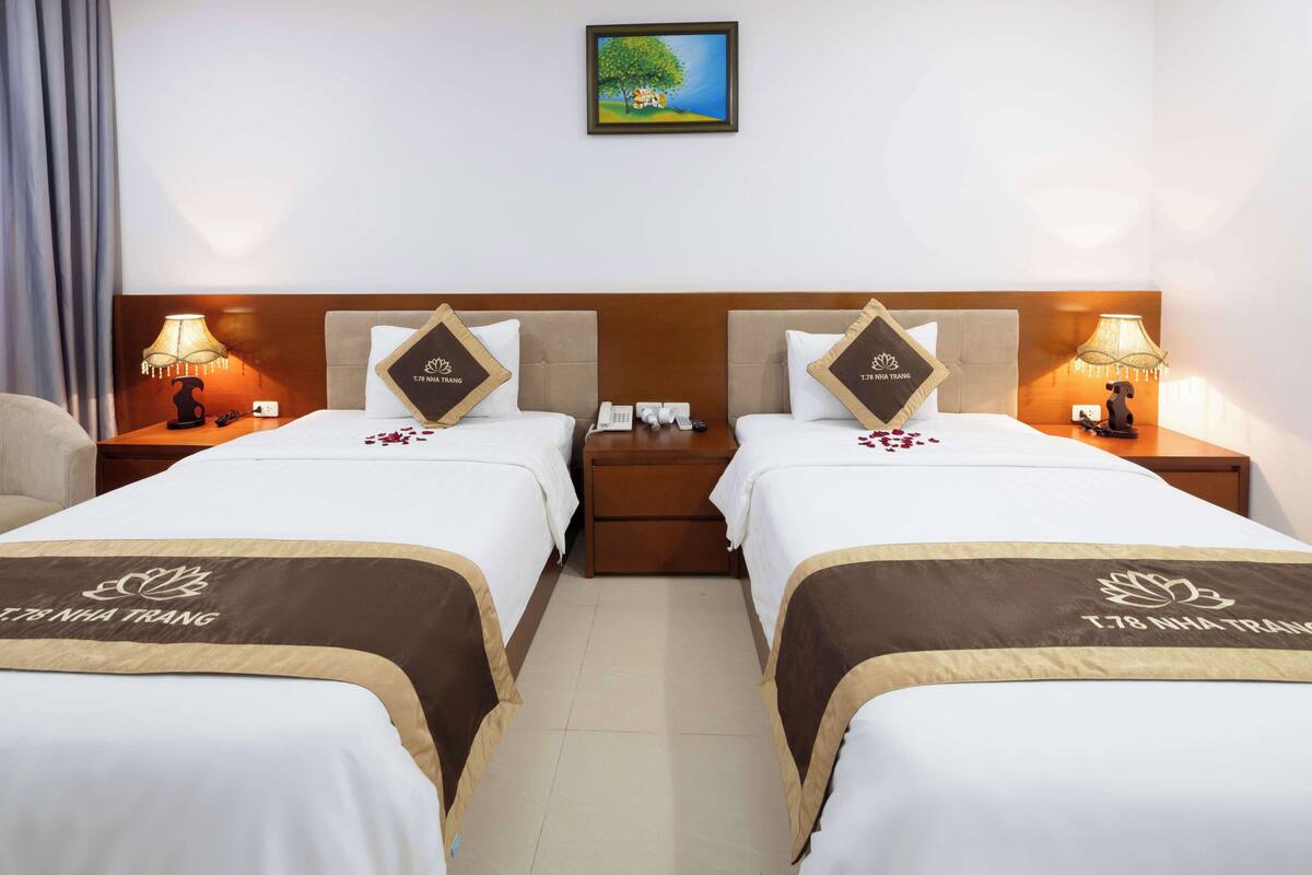 A hotel room with two beds, each with a headboard, bedside tables with lamps, a nightstand, and a framed picture on the wall.